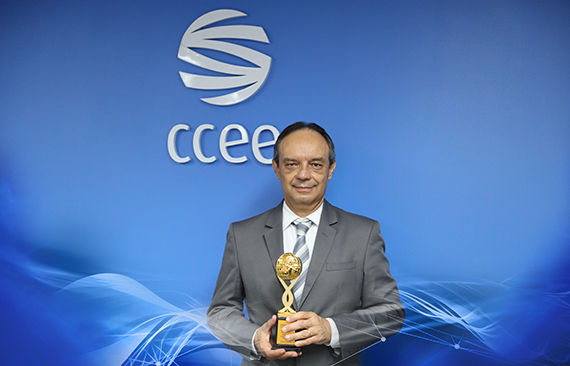 Imagem mostra o presidente do Conselho de Administração da CCEE, Rui Altieri, segurando um troféu dourado. Ele é um homem branco, de meia idade, e veste um terno cinza, com camisa branca e gravata listrada azul e branca. 