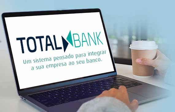 Notebook com o texto Total Bank, uma mão digitando e outra segurando o copo de café