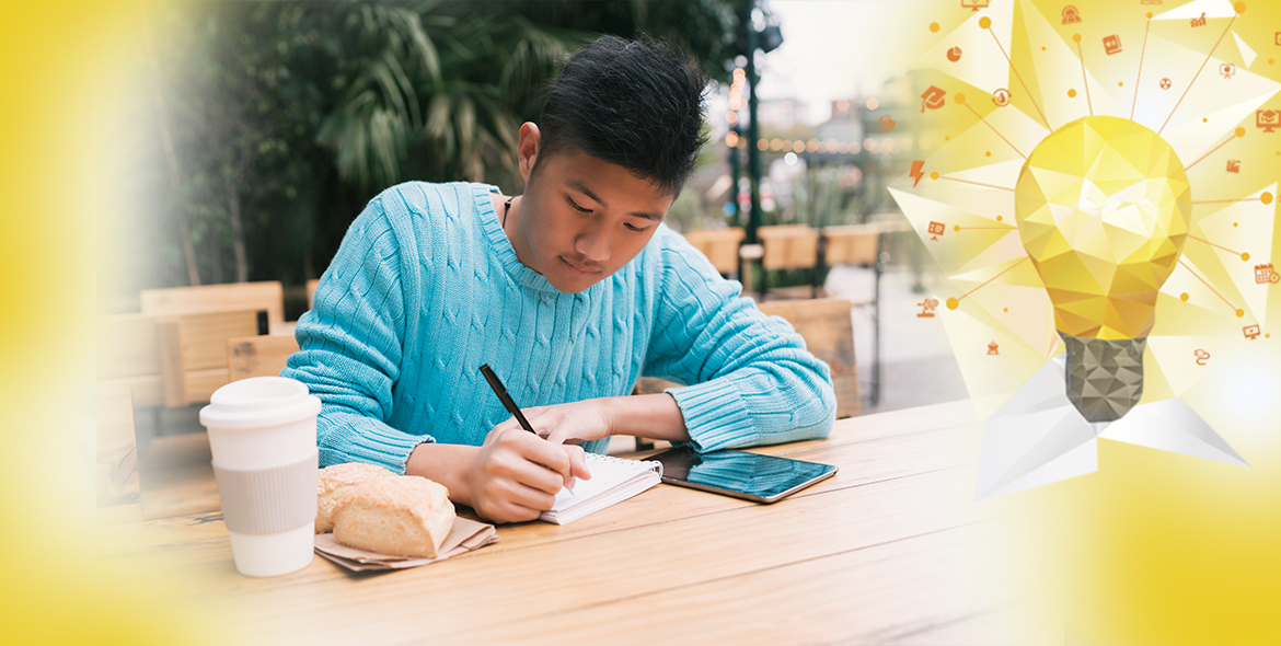 Imagem mostra um homem pardo, sentado em frente a notebooks e cadernos, que escreve algo