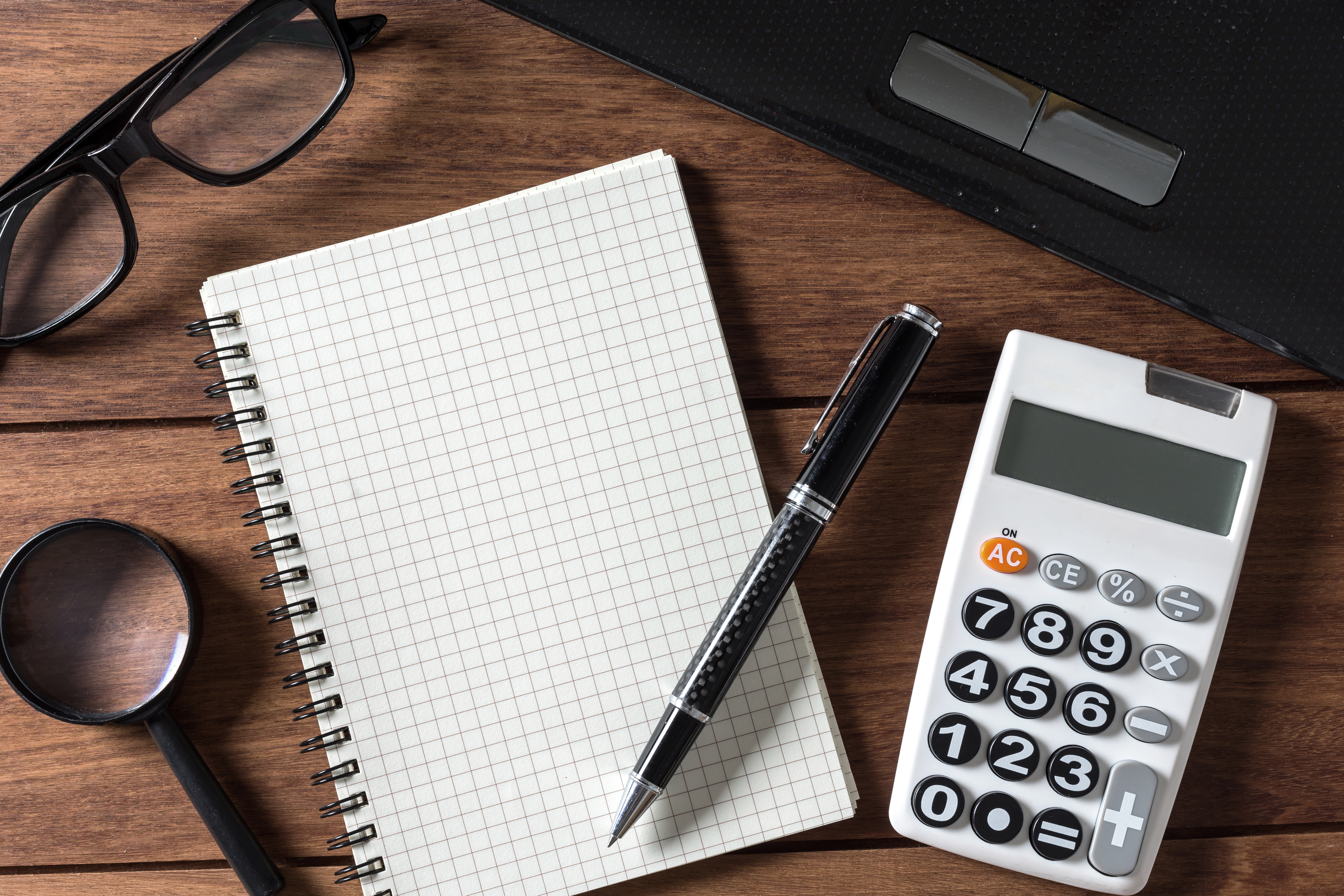 Imagem mostra uma calculadora e um caderno sobre uma mesa de madeira