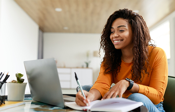Imagem mostra uma mulher negra, de camiseta laranja, estudando em frente a um computador