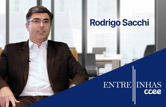 A imagem mostra Rodrigo Sacchi em um escritório. Ele é um homem branco, de cabelos pretos, e veste um paletó preto.