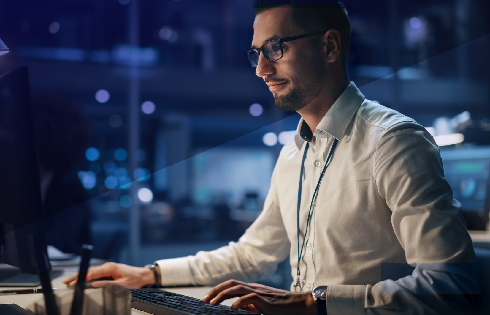 A imagem mostra um homem branco, de camisa, em frente ao seu computador