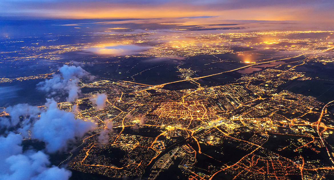 Imagem aérea de uma cidade iluminada, durante o anoitecer