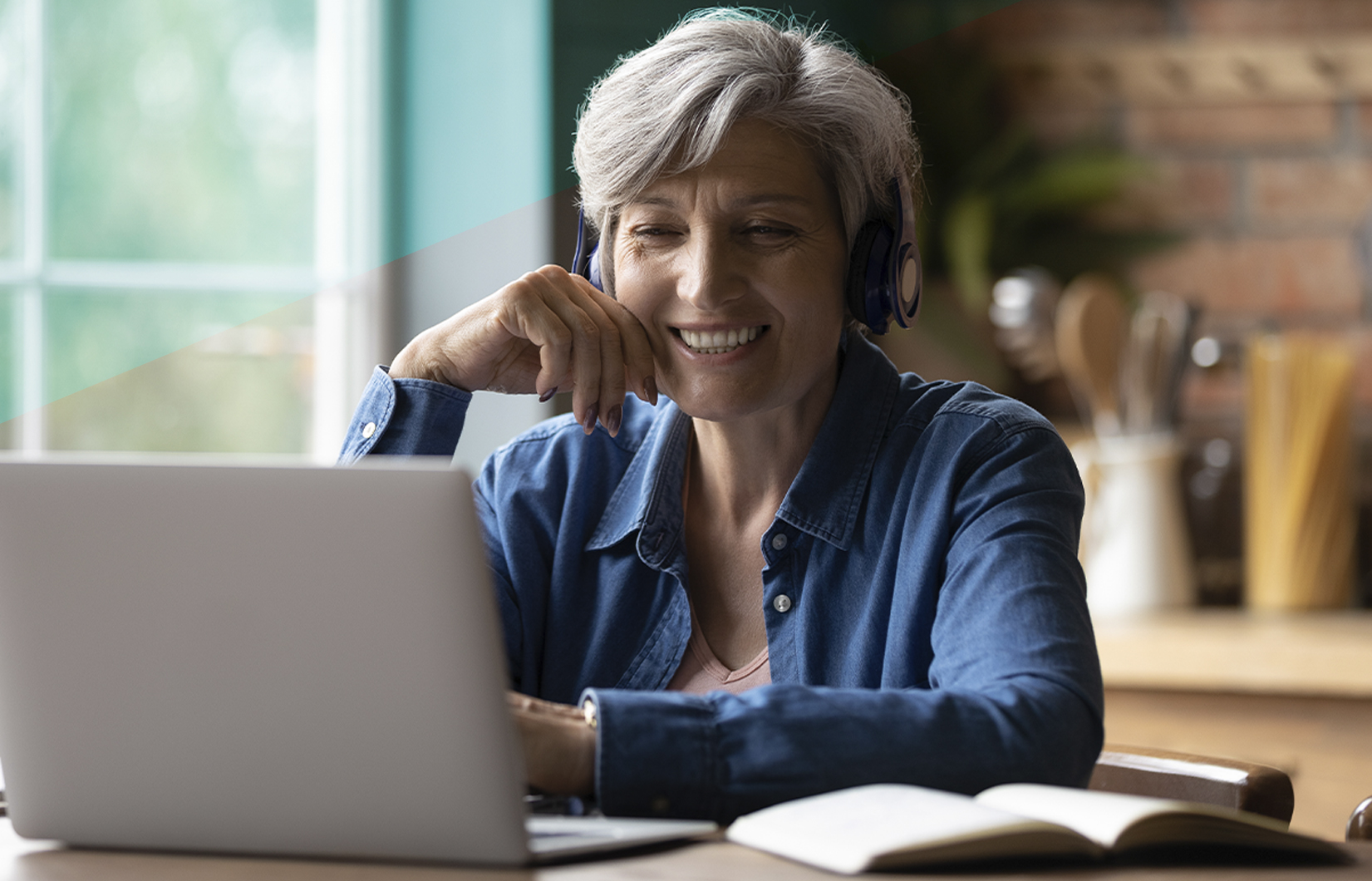 A imagem mostra uma mulher grisalha em frente a um computador. Ela veste uma camisa azul e sorri.