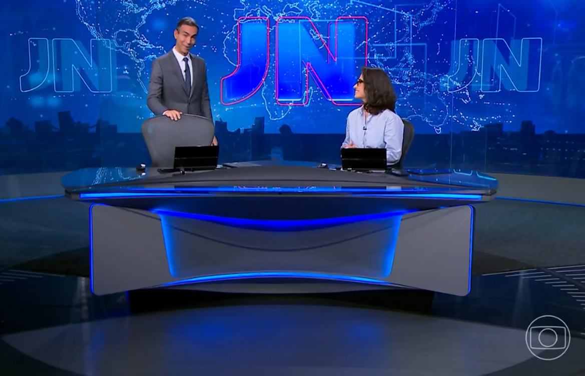 A imagem mostra os apresentadores César Tralli e Renata Vasconcellos na bancada do Jornal Nacional